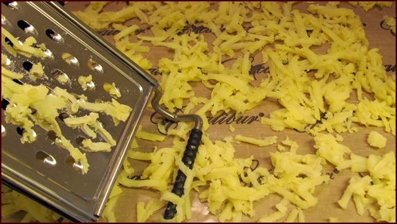 Grating potatoes on nonstick sheet for dehydration.