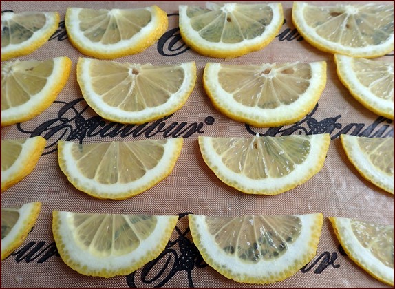 Sliced lemons cut in half on nonstick sheet.